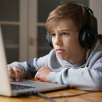 Мальчик задумчиво смотрит в экран ноутбука в наушниках